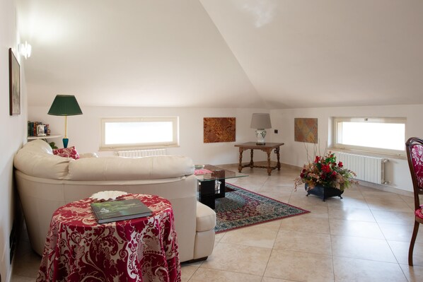 A living room with a sofa, a small table with a book, a lamp, a coffee table, a rug, and a flower arrangement.