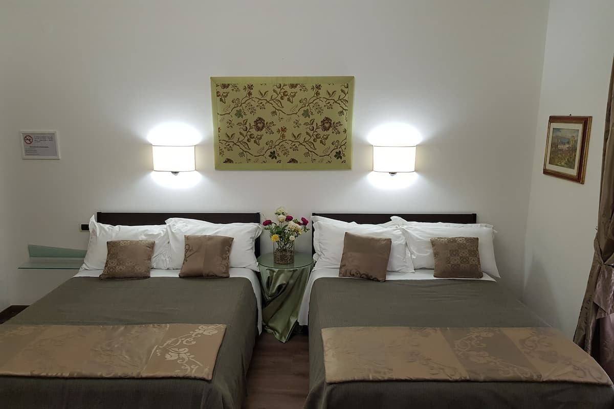 Une chambre d’hôtel avec deux lits simples, chacun recouvert d’une couvre-lit verte et agrémenté d’oreillers assortis. Une petite table avec un vase de fleurs se trouve entre les deux lits.