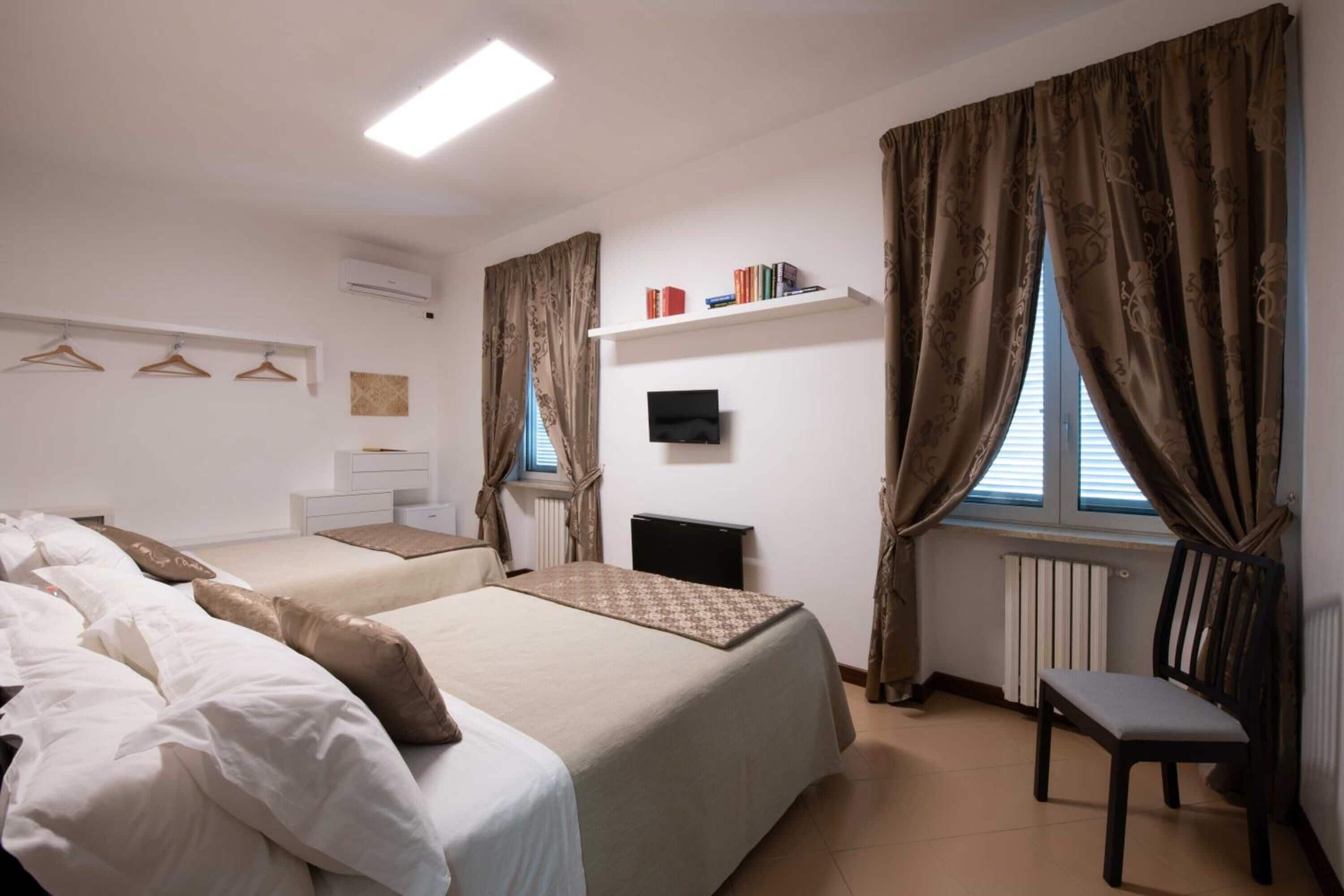 Una camera da letto con due letti, una scrivania, una sedia, un televisore e una finestra con tende.