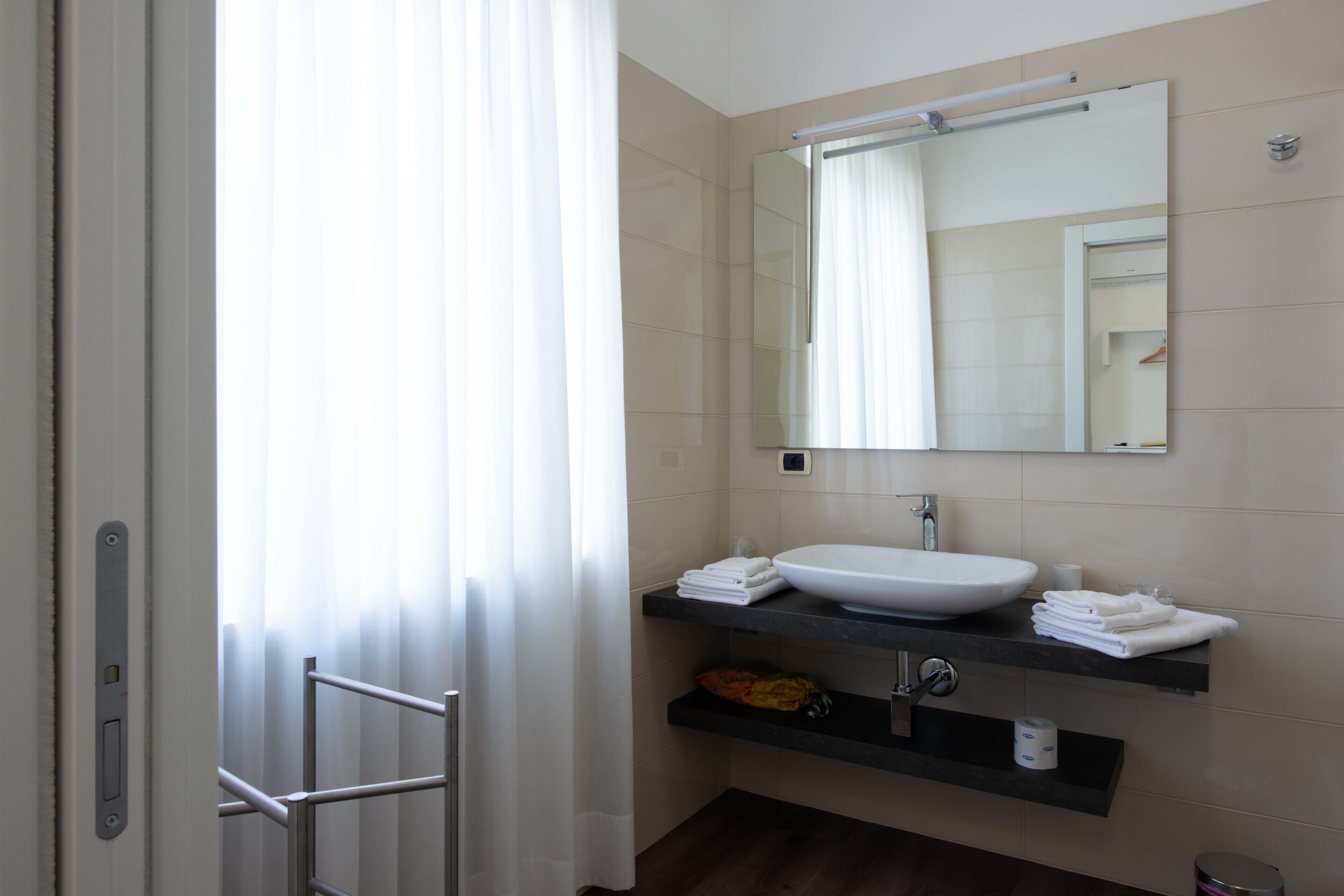 A modern bathroom with a white sink, a large mirror, and a towel rack.