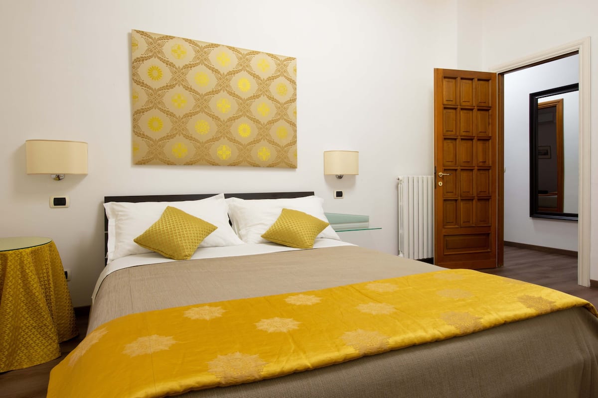 Une chambre d’hôtel avec un lit, deux lampes de chevet, un radiateur et une porte en bois.