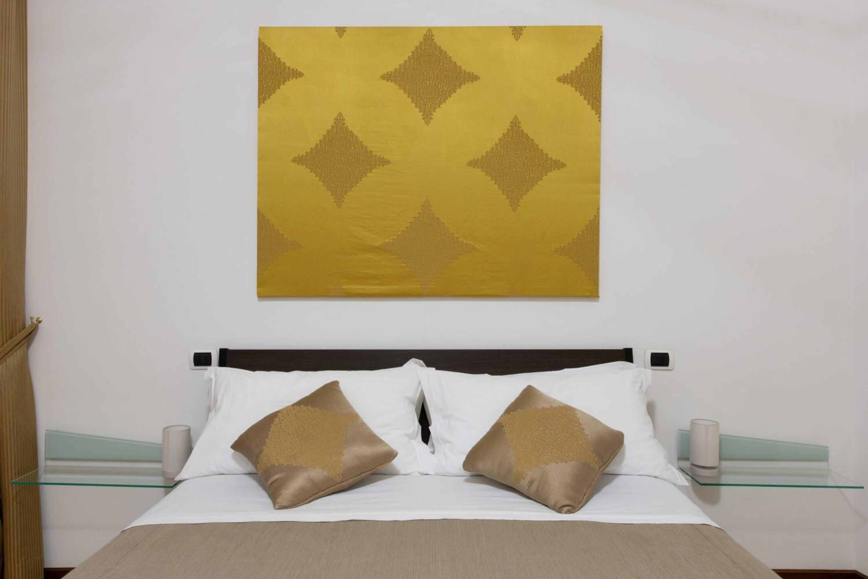A hotel room with a bed, two bedside tables, a nightstand, and a wall-mounted artwork.