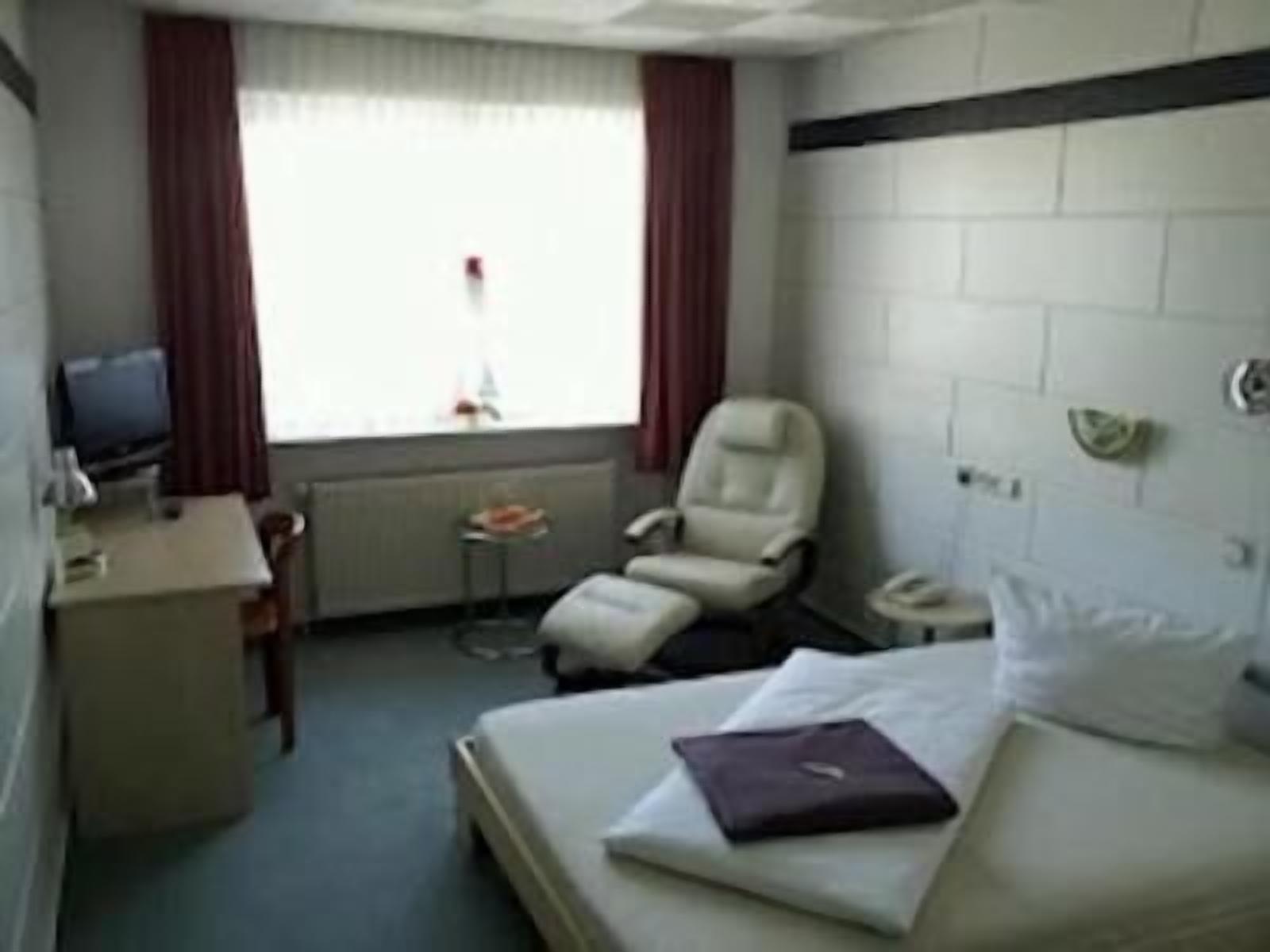 A hotel room with a bed, a desk, a chair, a television, and a window with curtains.