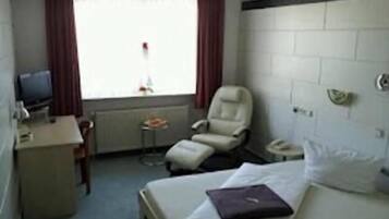 A hotel room with a bed, a desk, a chair, a television, and a window with curtains.