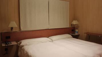 Een hotelkamer met een groot bed, twee nachtkastjes met lampen, en een groot raam met zonwering.
