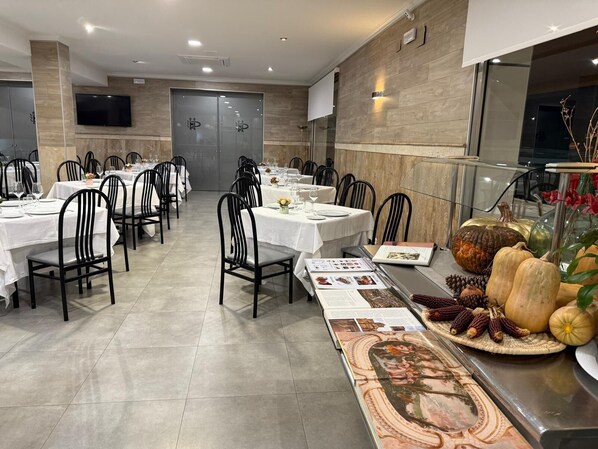 Un espace repas comprenant plusieurs tables, des chaises et un long panneau présentant le menu.