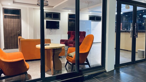 Un intérieur moderne avec une cloison en verre, des chaises orange, une table en bois et un téléviseur à écran plat fixé au mur.