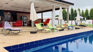 Un espace aménagé au bord de la piscine, avec des chaises longues et des parasols, un coin salon abrité et une piscine à l’eau d’un bleu limpide.