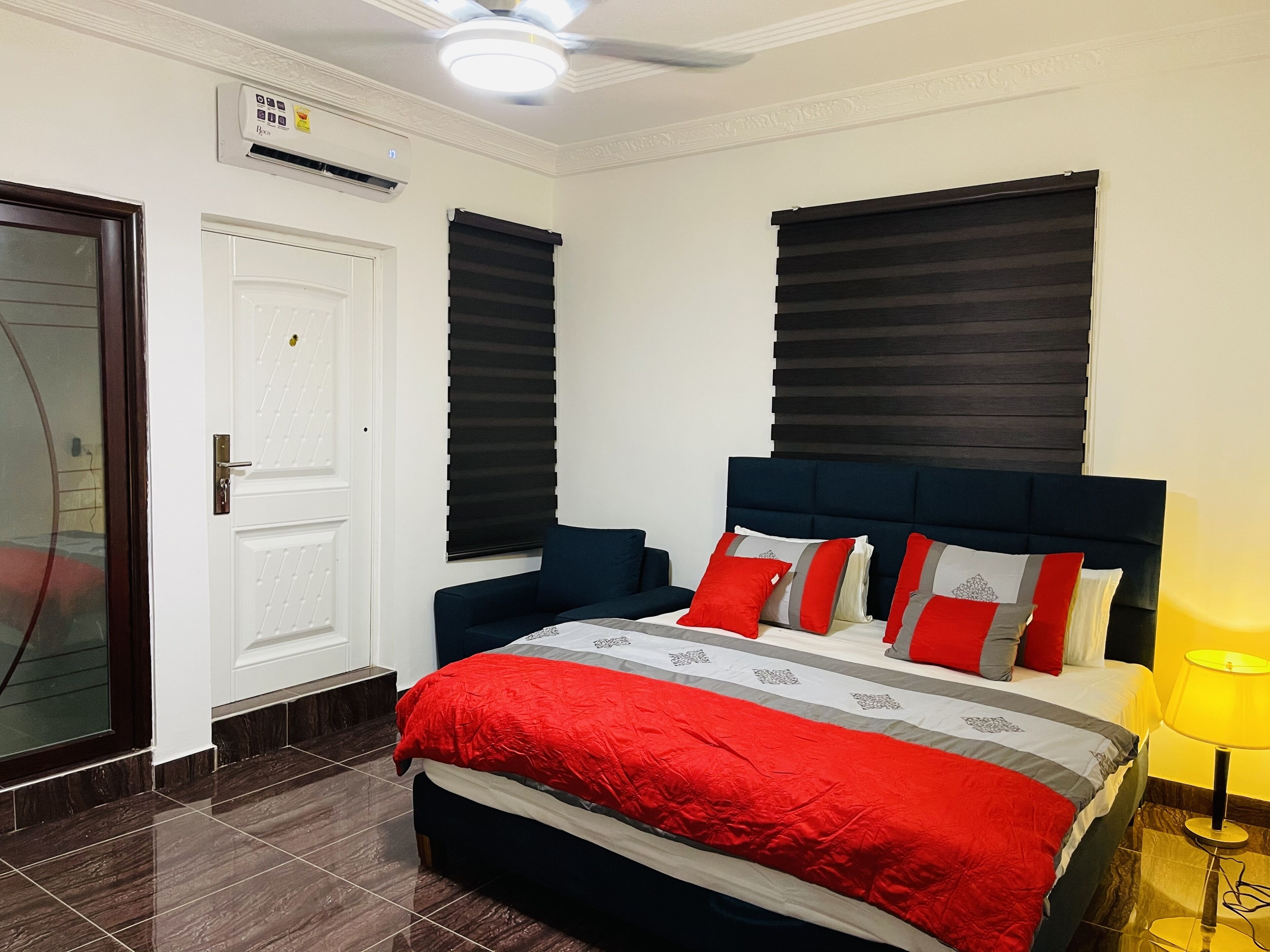 A bedroom with a bed, a bedside table, a lamp, a ceiling fan, and a door.