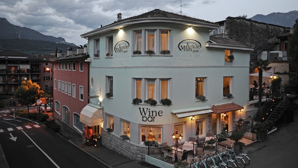 Um edifício com um bar de vinhos no andar térreo, com mesas ao ar livre e uma escadaria que dá acesso aos andares superiores.