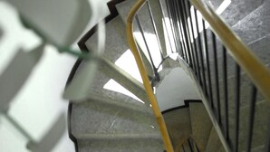 Uma escadaria em espiral com corrimão, um quadro na parede e uma janela no topo.