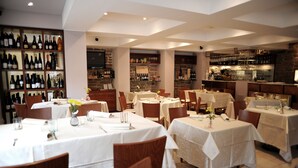 Restaurante com várias mesas preparadas para refeições, um espaço para vinhos à esquerda e uma área de bar à direita.