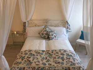 Una cama con dosel, ropa de cama blanca y almohadas estampadas con motivos florales.