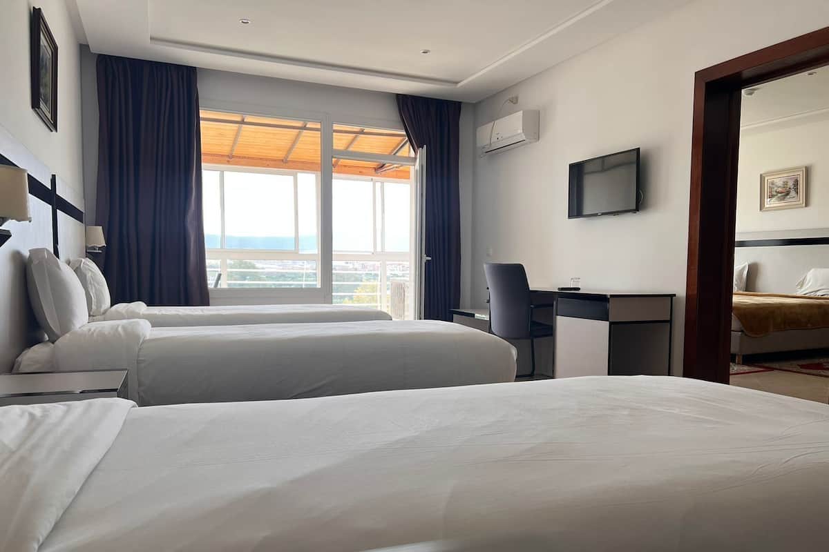 Ein Hotelzimmer mit zwei Betten, einem Schreibtisch, einem Stuhl, einem Fernseher und einem Fenster mit Vorhängen.