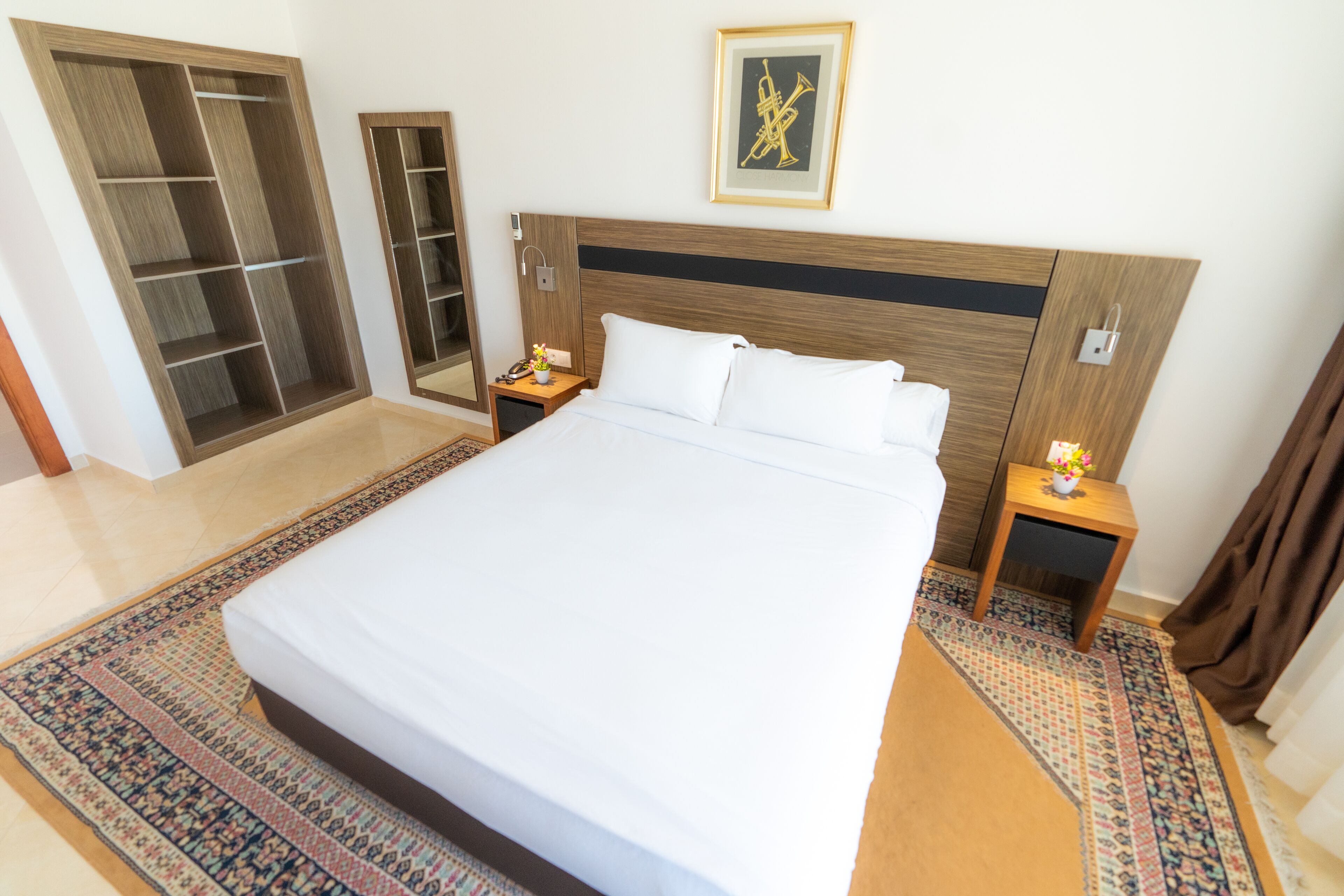 A hotel room with a large bed, a wardrobe, a bedside table with a lamp, and a framed picture on the wall.