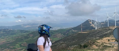 Una persona en un cuatrimoto en una zona rural, con aerogeneradores al fondo.
