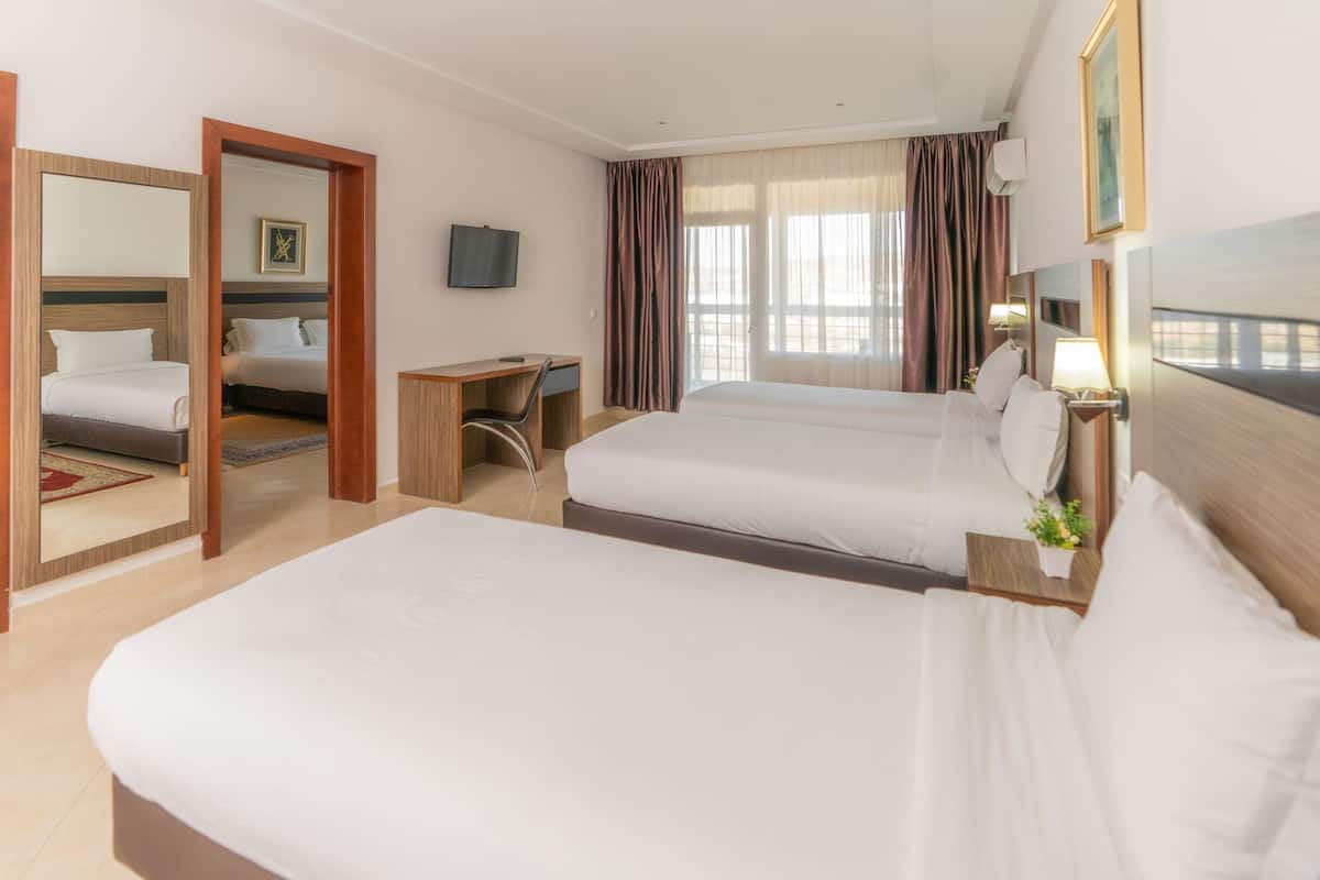 Ein Hotelzimmer mit zwei Betten, einem Schreibtisch, einem Fernseher und einem Vorhangfenster.