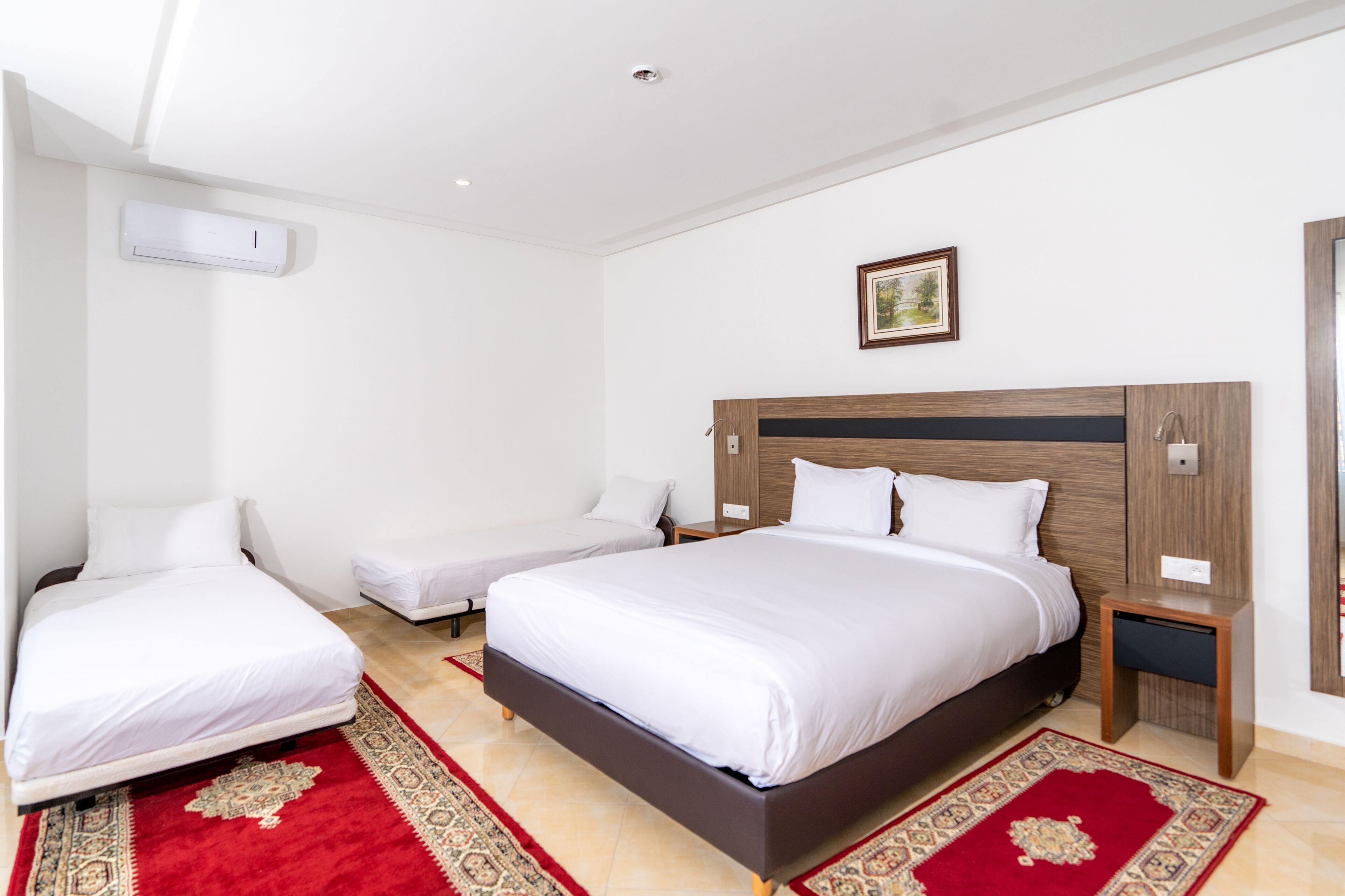 Una camera d'albergo con un letto grande, un letto più piccolo, un comodino e un condizionatore d'aria a parete.