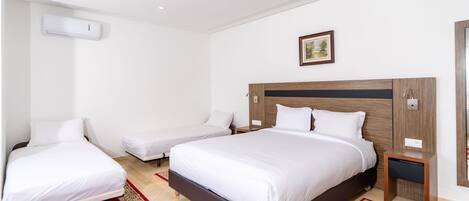 Una camera d'albergo con un letto grande, un letto più piccolo, un comodino e un condizionatore d'aria a parete.