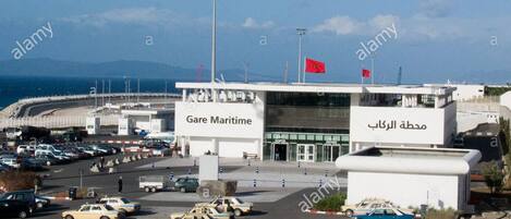 A parking lot with several cars, a building labeled "Gare Maritime," and a sign with Arabic text.