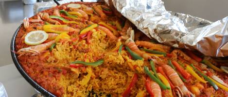 Una paella grande con gambas, pimientos y rodajas de limón.