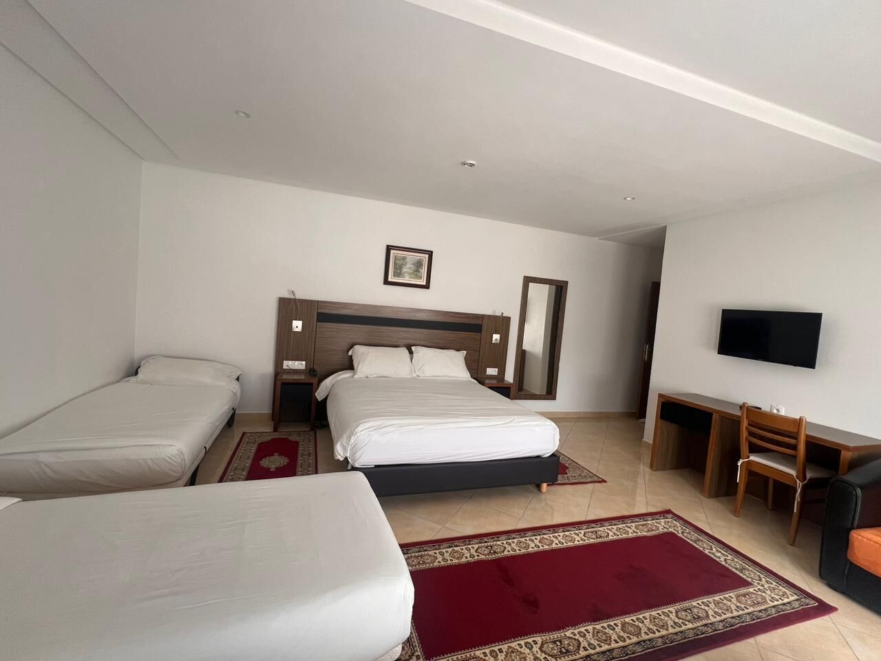 Een hotelkamer met twee eenpersoonsbedden, een groter bed, een televisie, een bureau en een stoel.