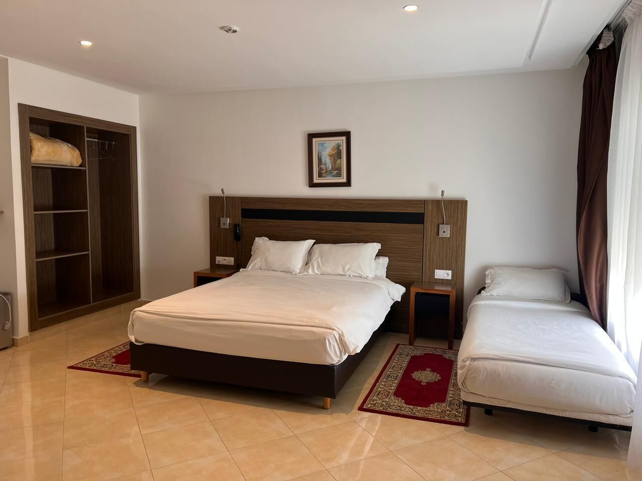 Una habitación de hotel con una cama grande, una cama más pequeña, un armario y un cuadro en la pared.