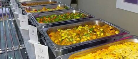 Un bufé con diversos platos, incluyendo un curry de pollo y un guiso de patatas.