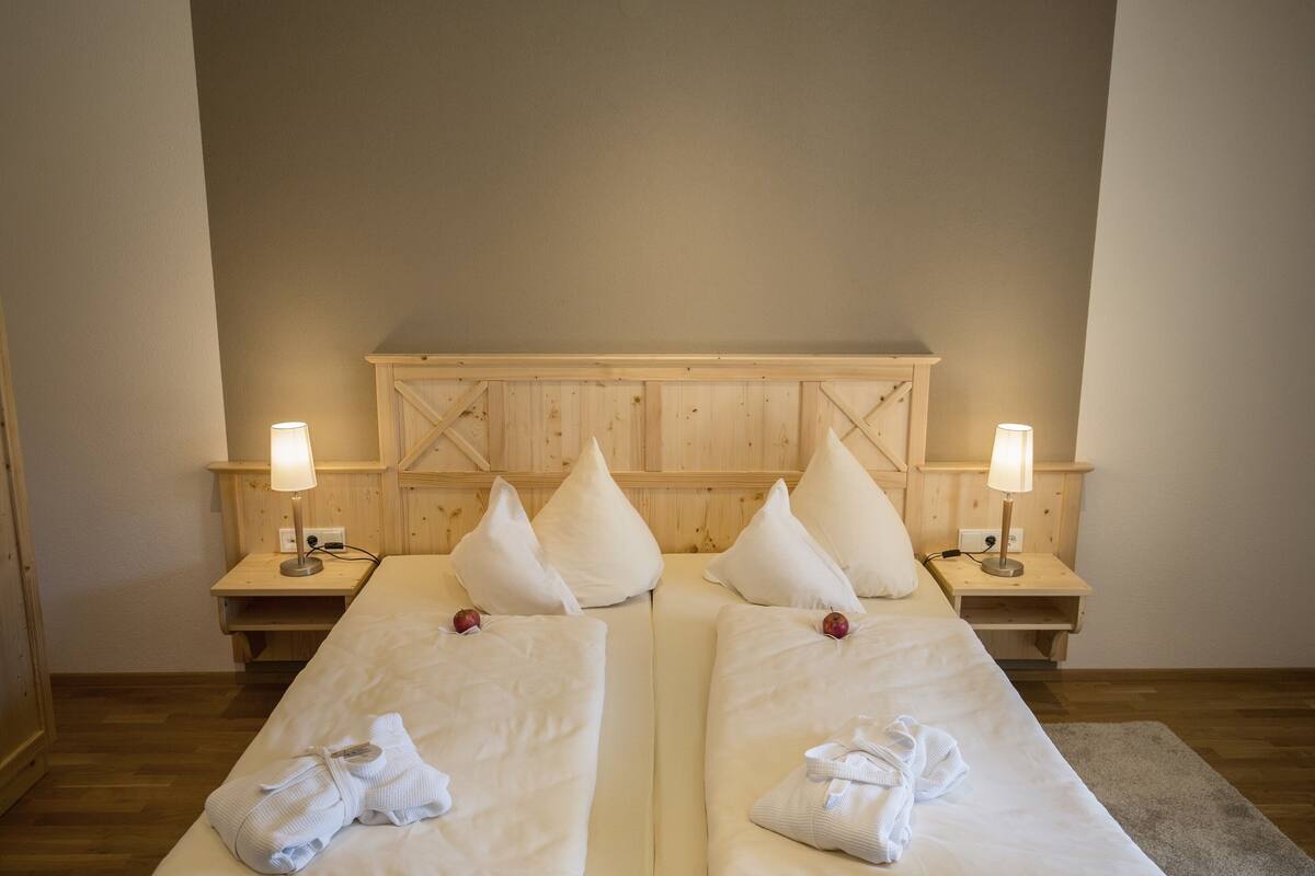 Habitación doble con dos camas, cabecero de madera, lámparas de noche y toallas sobre las camas.