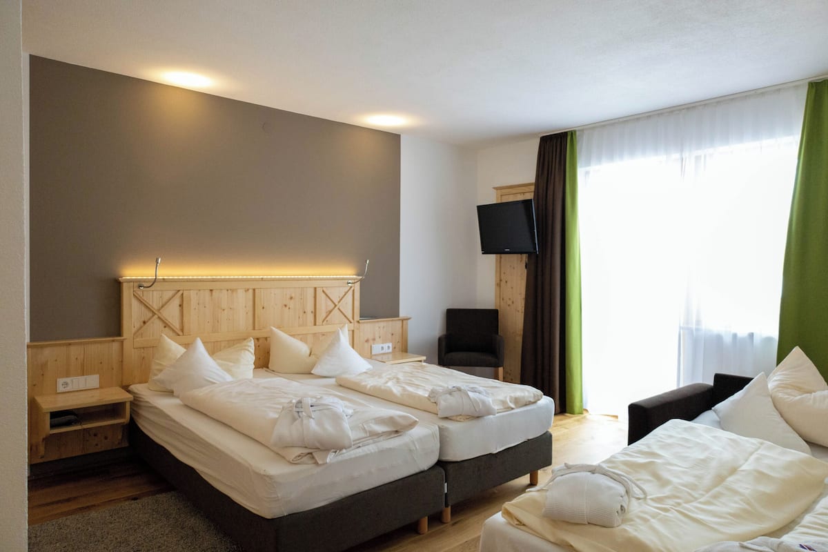 Habitación de hotel con dos camas, televisión, una silla y una ventana con cortinas.
