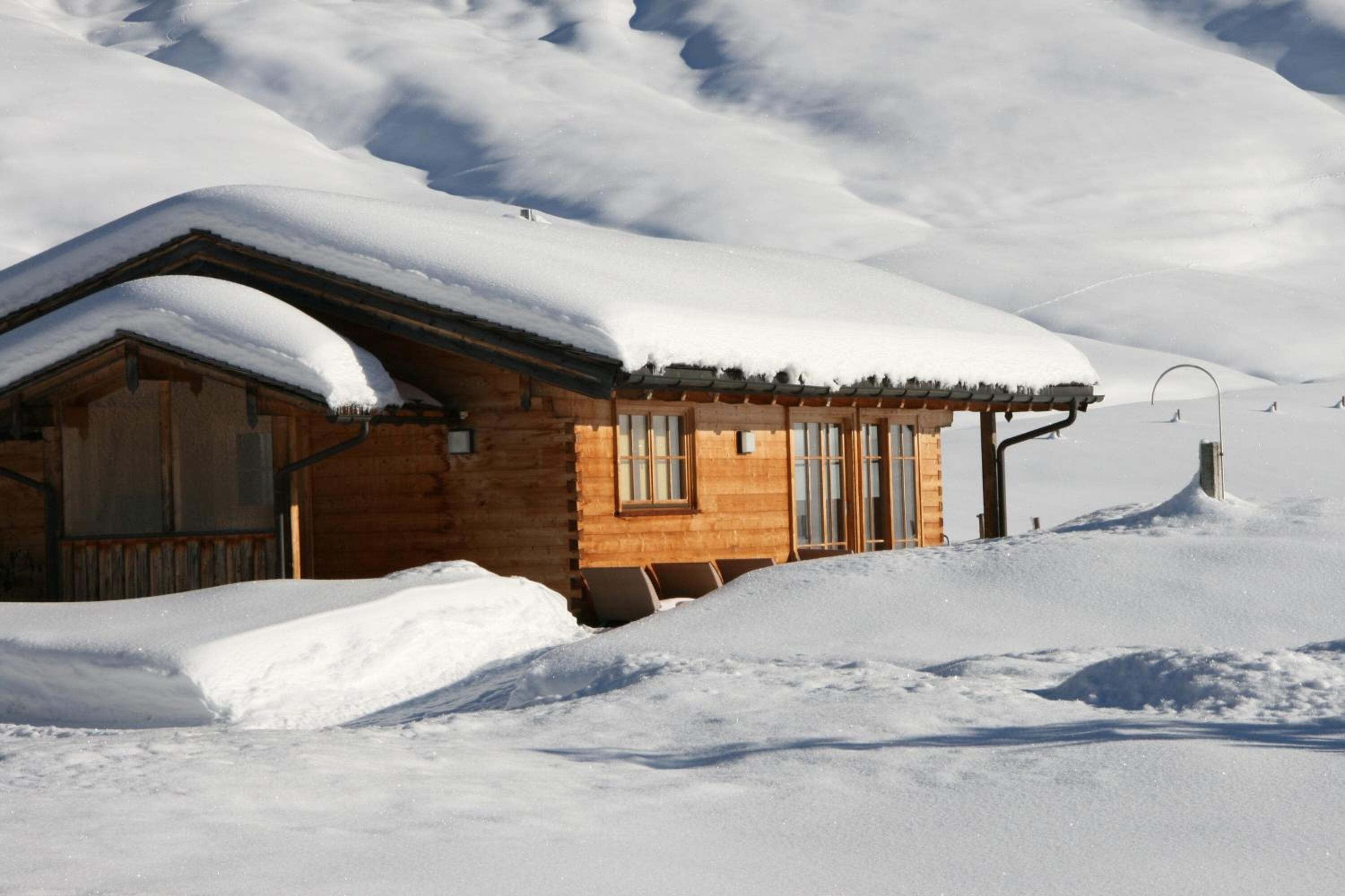 Een houten chalet met een sneeuwbedekte dak, omgeven door besneeuwde grond en bergen op de achtergrond.