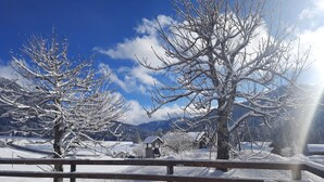 A snow-covered landscape with a wooden fence, a small wooden structure, and mountains in the background.