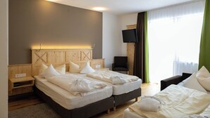 A hotel room with two beds, a TV, a chair, and a window with curtains.