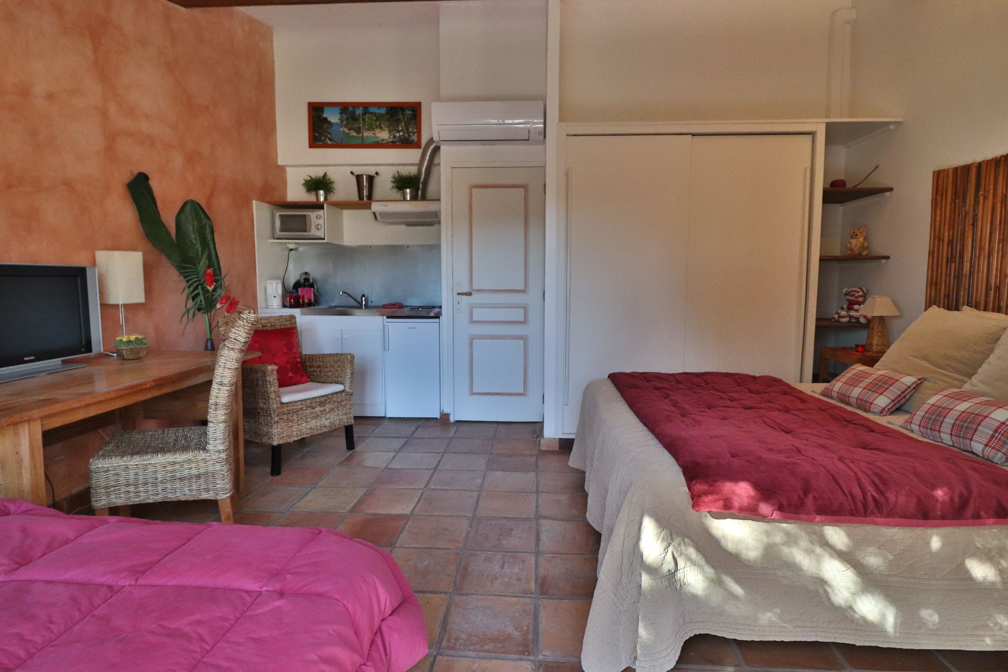 Una habitación compacta con cama, una silla, escritorio y kitchenette.
