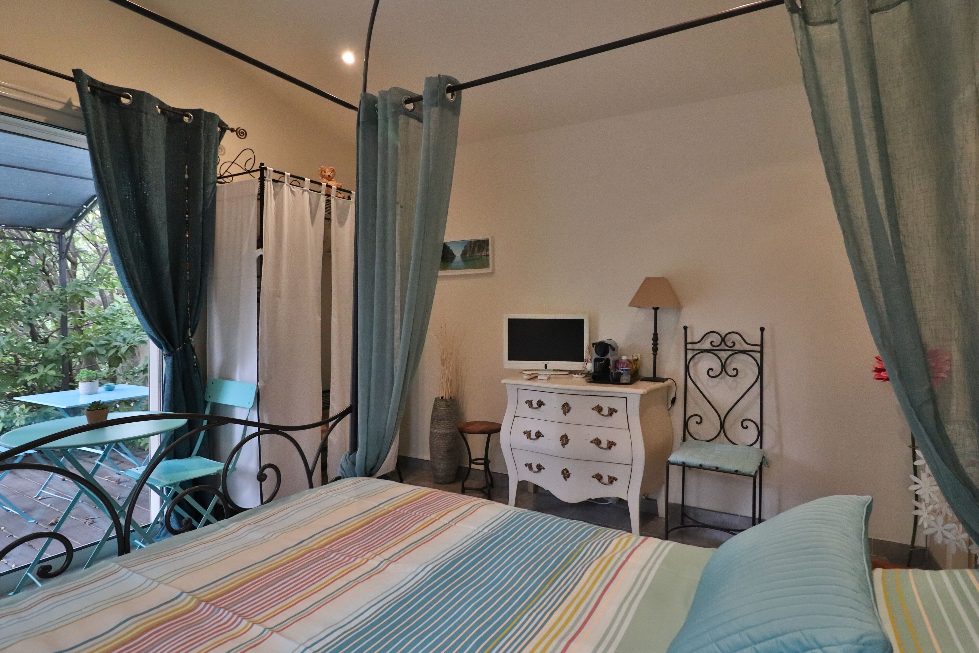Une chambre à coucher avec un lit, une commode, une chaise, une table et une fenêtre avec des rideaux.