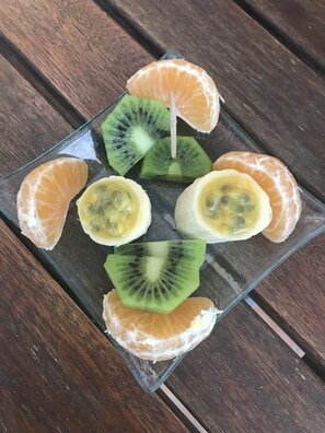 A glass plate with sliced kiwi and orange segments on a wooden table. - Le Mas de Bertagne - Chambres d'Hôtes (Gemenos)