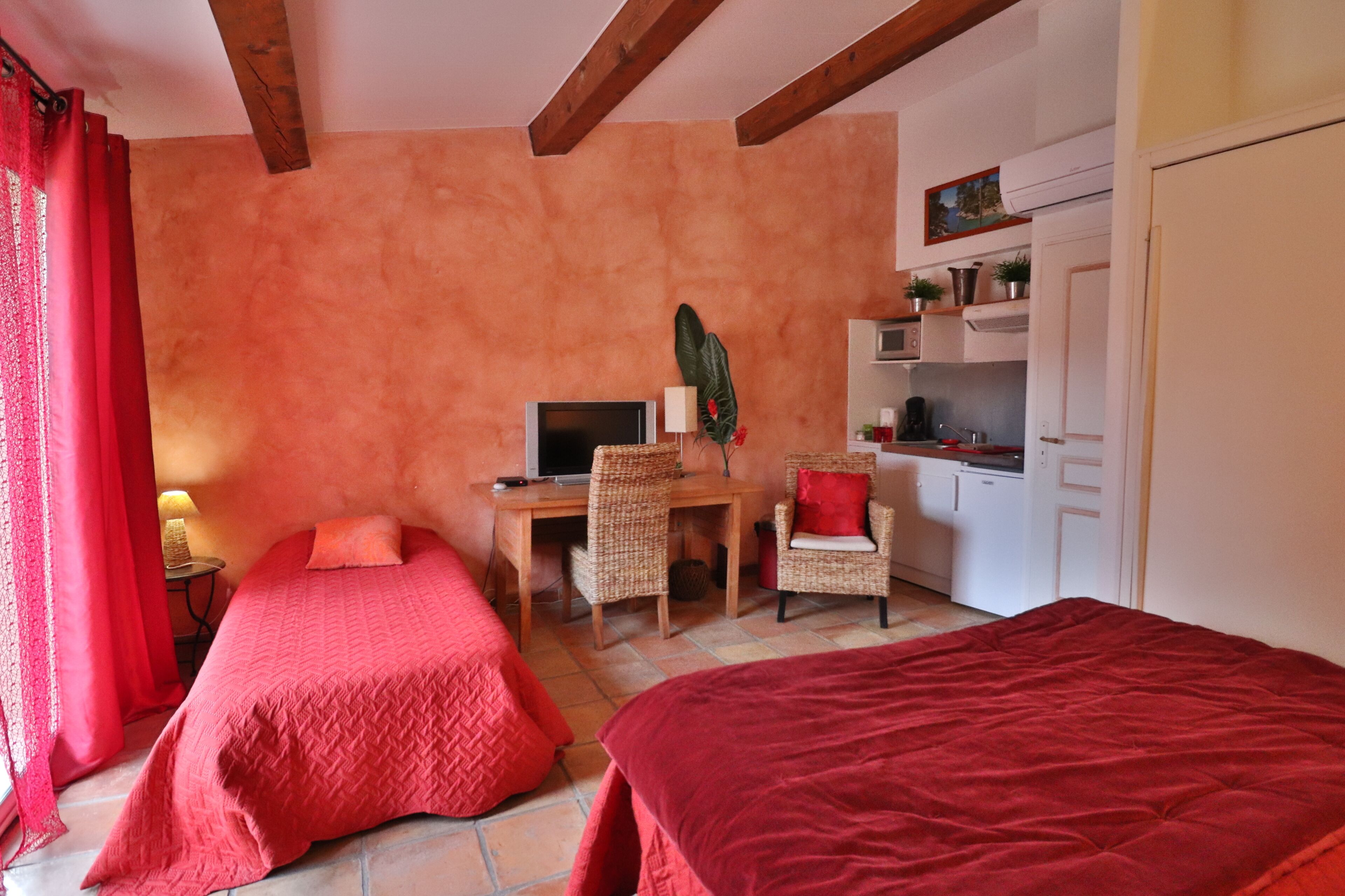 Una habitación con dos camas, un escritorio, una silla, un televisor y una kitchenette.