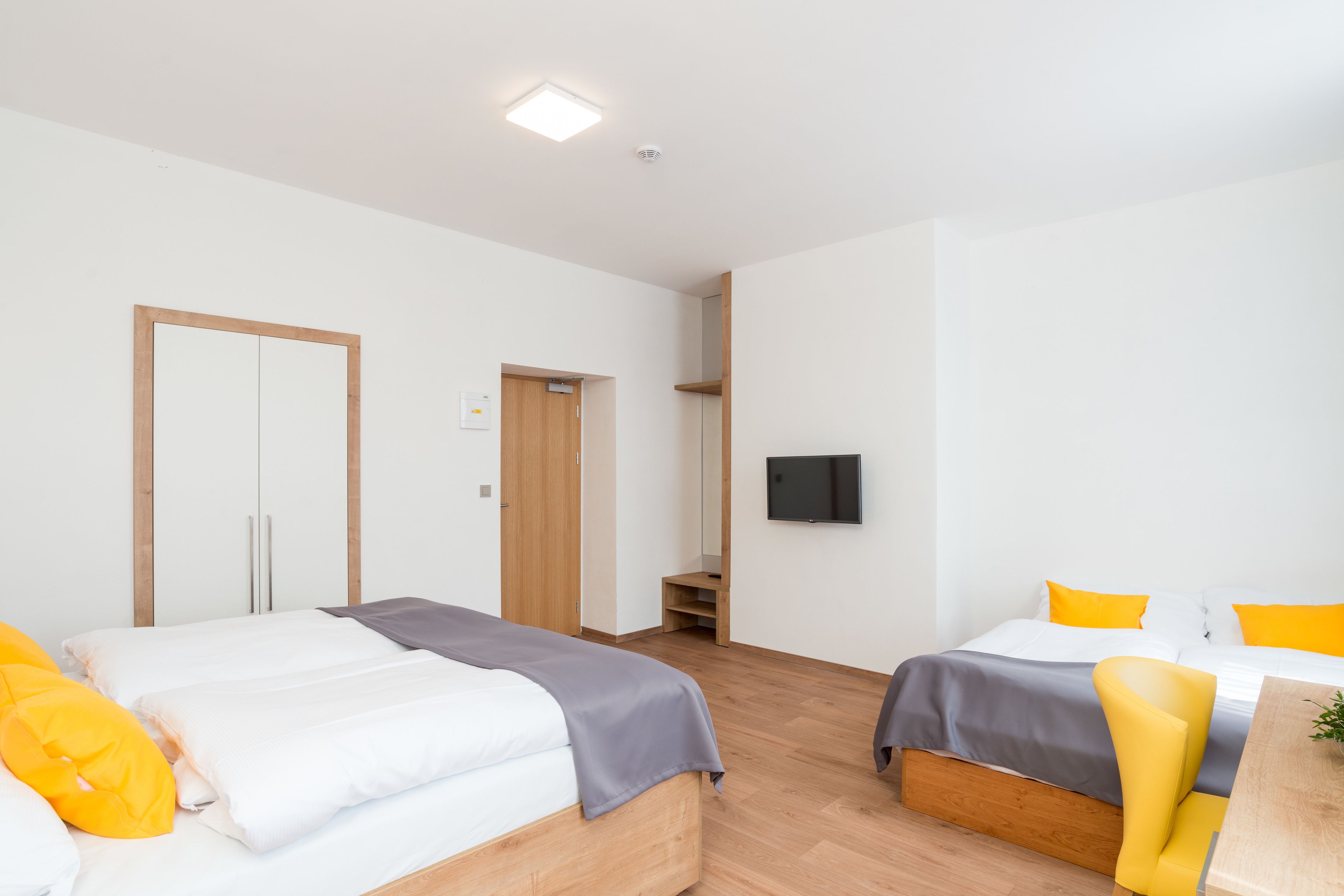 Habitación de hotel moderna con dos camas, piso de madera, un televisor de pantalla plana y un escritorio pequeño.