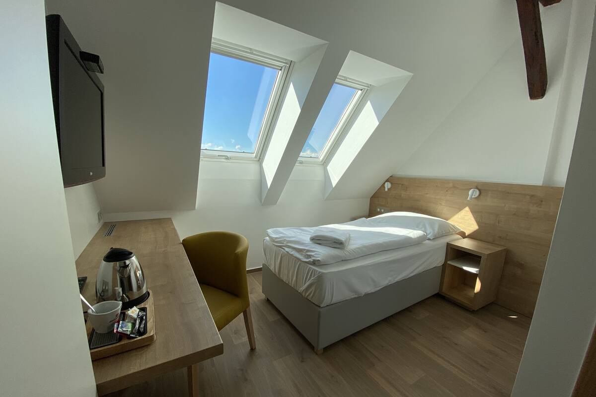 A bedroom with a bed, a desk, a chair, and two skylights.