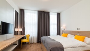 Een hotelkamer met een bed, een bureau met stoel, een televisie en een raam met gordijnen.