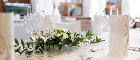 Una mesa dispuesta con copas de vino, un centro de mesa con flores blancas y un posavasos decorativo.