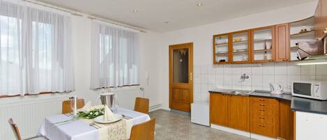Comedor con mesa preparada para cuatro, cocina con armarios de madera y un microondas, y una puerta que da a otra habitación.