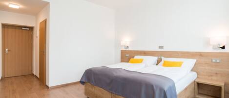 A modern hotel room with a wooden bed, white walls, and a wooden floor.