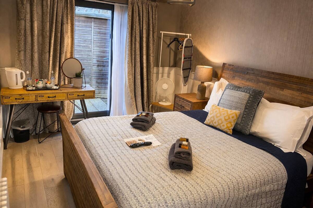 Una habitación de hotel con cama, escritorio, silla, espejo, lámpara y ventana con cortinas.