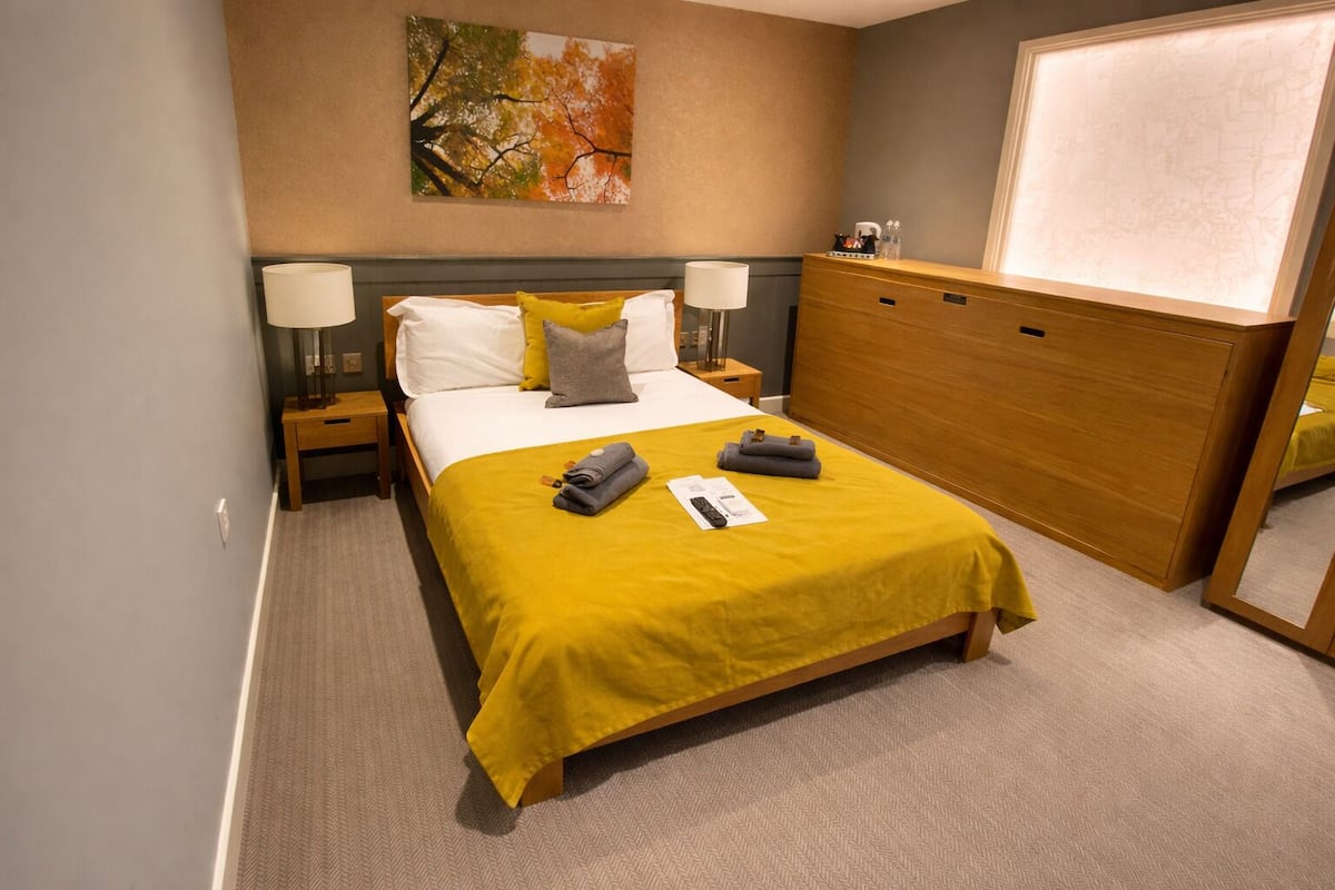 Habitación de hotel con cama, mesitas de noche, cómoda de madera, un cuadro en la pared y un mapa sobre la cómoda.