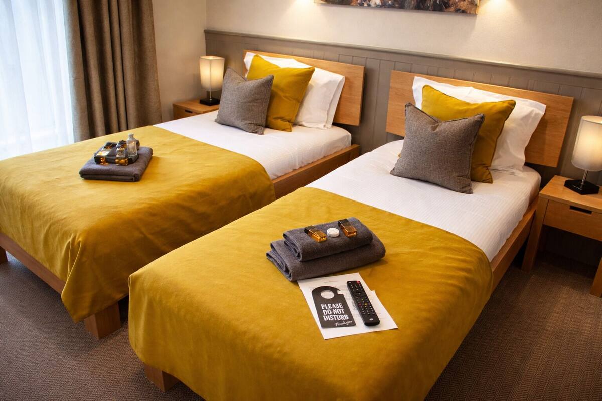 Dos camas matrimoniales con ropa de cama amarilla, mesitas de noche con lámparas y un cartel de 'No molestar' sobre las camas.