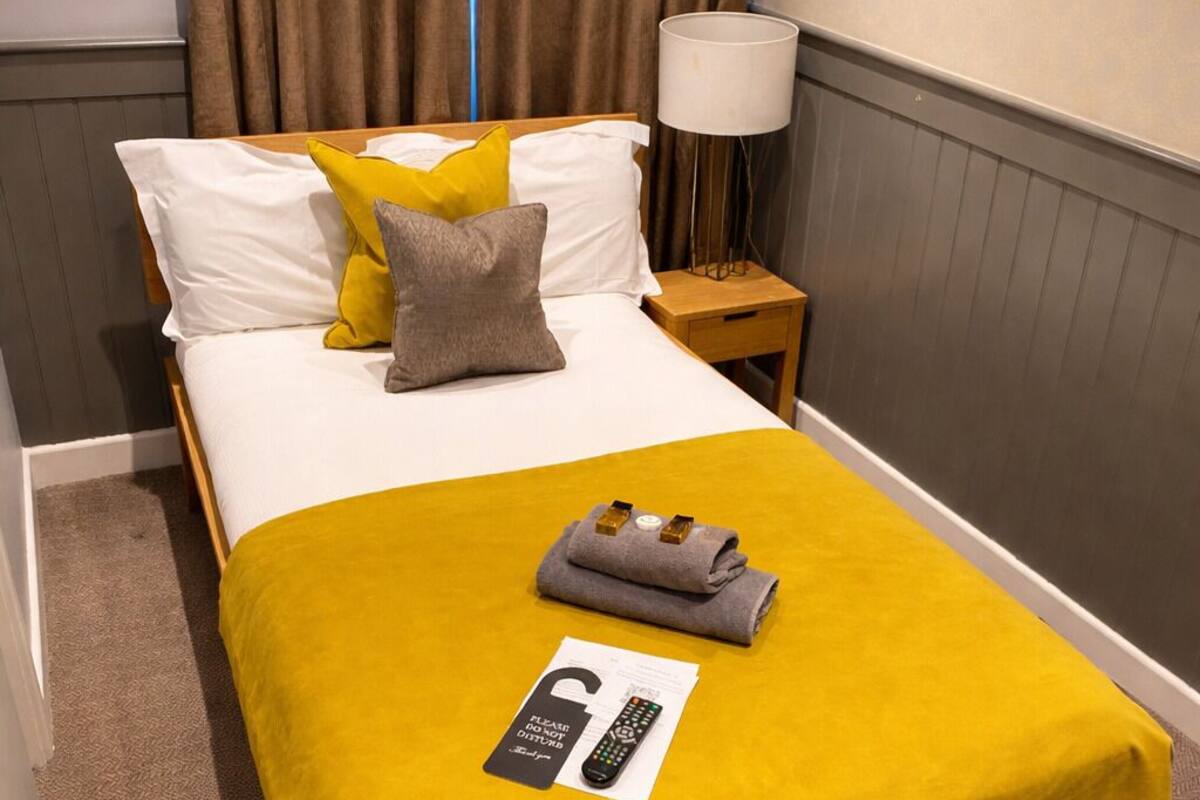 Habitación de hotel con una cama, una mesita de noche, una lámpara, un control remoto y un cuadro en la pared.
