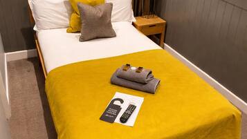 A hotel room with a bed, a nightstand, a lamp, a remote control, and a painting on the wall.
