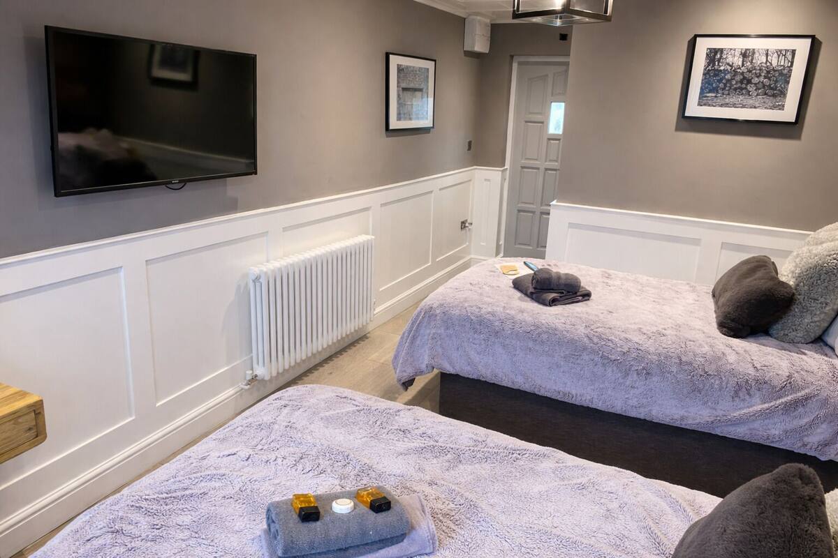 Habitación de hotel con dos camas, un radiador, un televisor y cuadros en la pared.