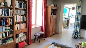A cozy living room with a wooden bookshelf filled with books, a small stool, and a table with a QR code.